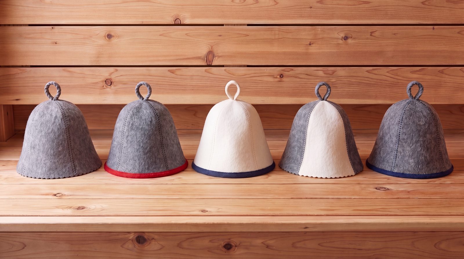 Five wool felt sauna hats in grey and white on a cedar shelf
